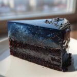 A slice of rich chocolate cake featuring a dark blue, galaxy-themed mirror glaze, resembling a night sky, perfect for a capricorn cake.