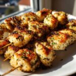 Close-up of golden brown Garlic Parmesan chicken skewers seasoned with herbs, served on a white plate.