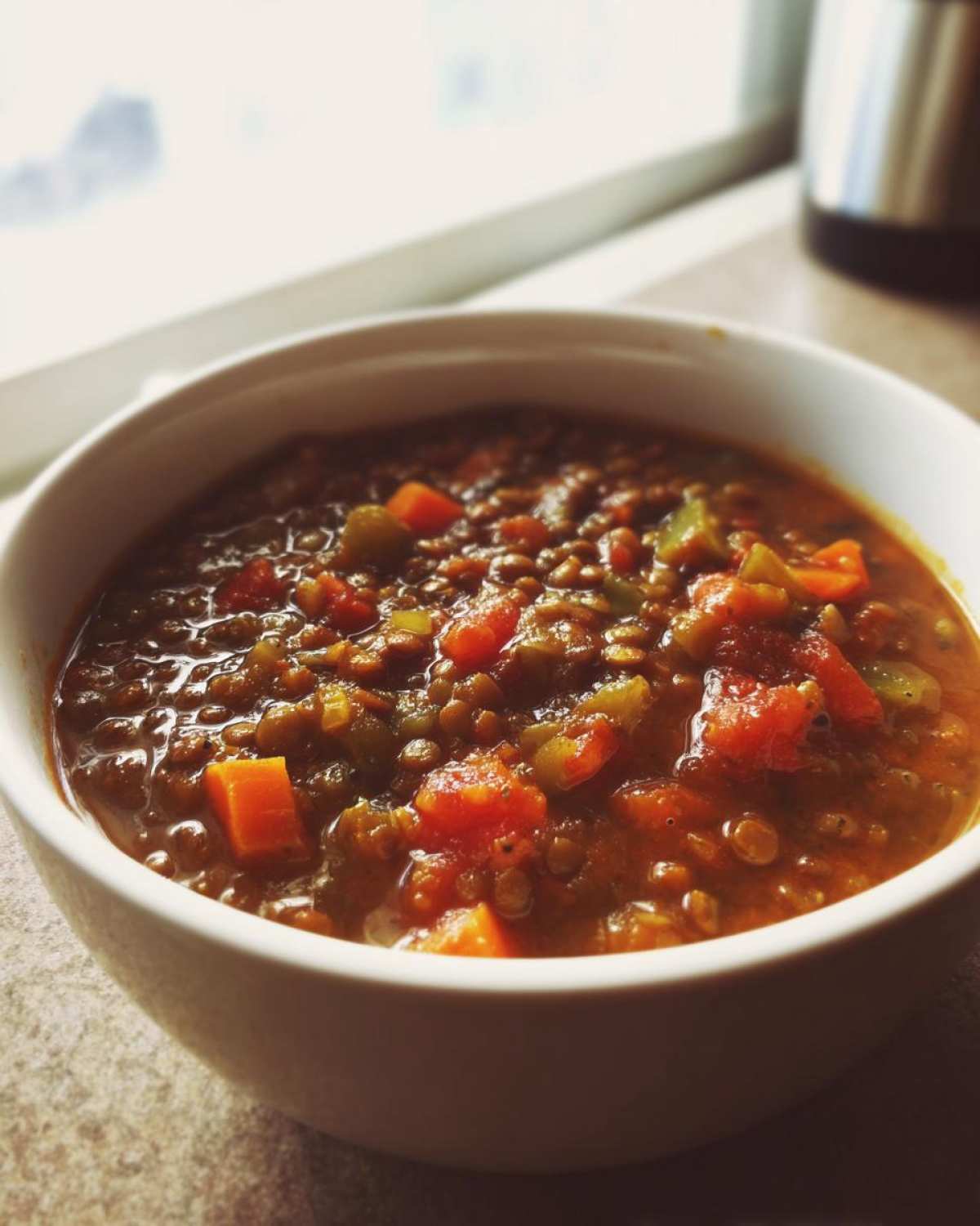 Close-up of a white bowl filled with thick, hearty lentil soup featuring visible chunks of carrots and celery.