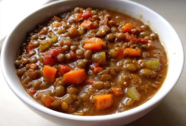Close-up of a thick, hearty lentil soup filled with diced carrots and celery in a white bowl.
