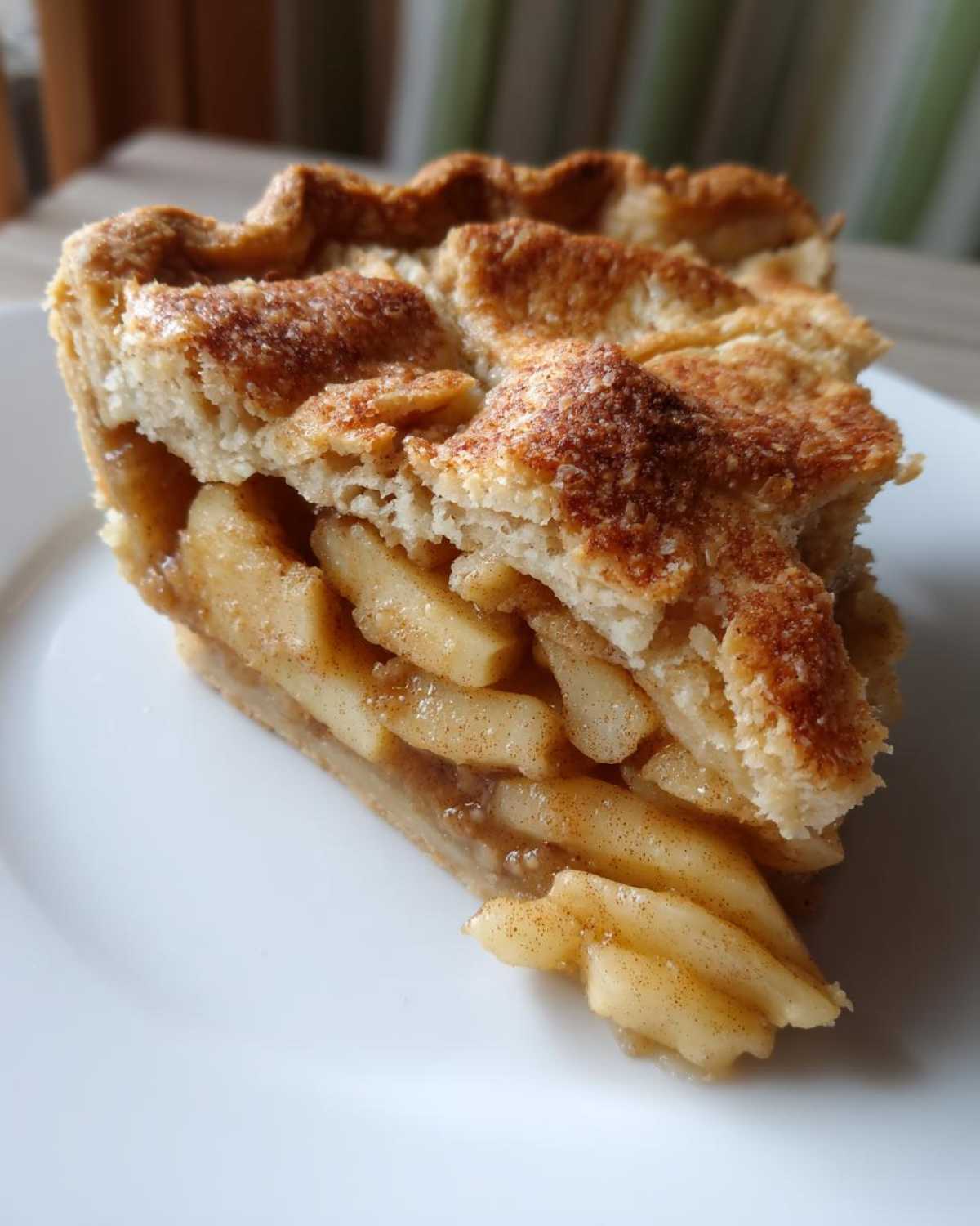 Close-up of a thick slice of homemade apple pie showing layered, cinnamon-coated apple filling and a flaky lattice crust.