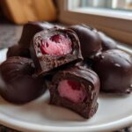 A pile of rich, dark chocolate covered cherries, with two cut open to show the bright red cherry filling inside.