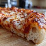 Close-up of a thick, airy slice of homemade pizza showing melted cheese and bubbly crust.