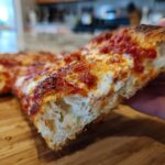 Close-up of a thick slice of homemade pizza showing the airy, bubbly crust, melted cheese, and rich tomato sauce.