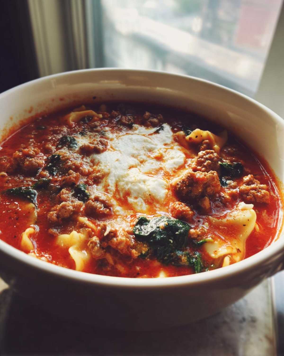 Close-up of a bowl of rich instant pot lasagna soup topped with dollops of white ricotta cheese and ground meat.