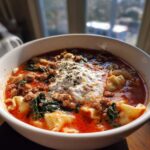 Close-up of a bowl of rich, red instant pot lasagna soup topped with a dollop of ricotta cheese and herbs.