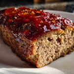 Close-up of a thick slice of juicy classic meatloaf topped with a shiny, thick red glaze.