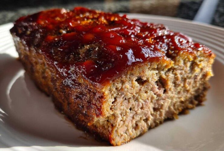 Close-up of a thick slice of juicy classic meatloaf topped with a shiny, thick red glaze.