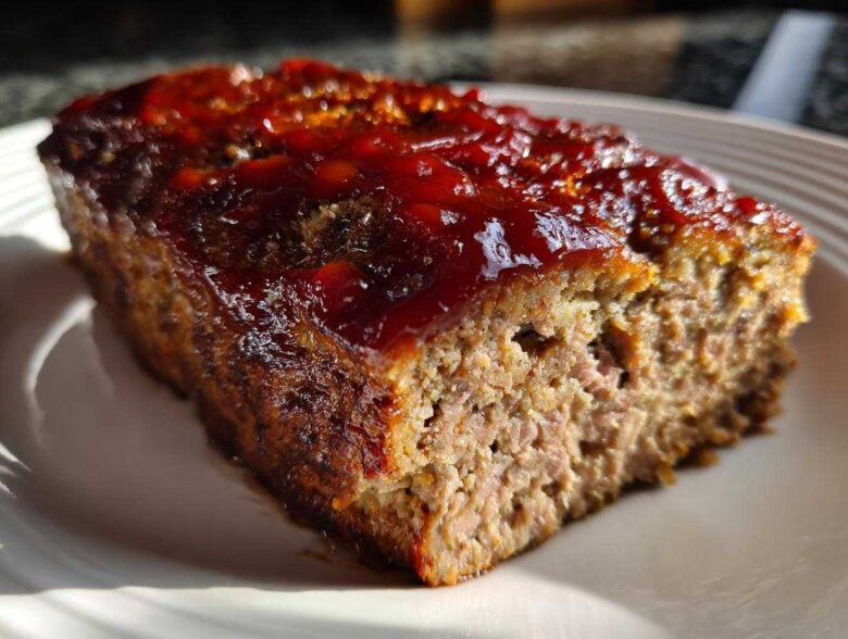 Close-up of a thick slice of juicy classic meatloaf topped with a shiny, thick red glaze.