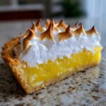 Close-up of a slice of lemon meringue pie showing bright yellow filling and torched meringue peaks.