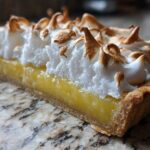 Close-up cross-section of a lemon meringue pie slice, showing bright yellow filling, crust, and fluffy, toasted meringue.