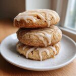Three soft maple brown sugar cookies stacked on a white plate, drizzled with a light glaze.