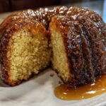 A slice cut from a moist Bacardi Rum Cake drizzled generously with a thick, amber caramel glaze.