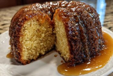 A slice cut from a moist Bacardi Rum Cake drizzled generously with a thick, amber caramel glaze.
