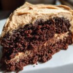 Close-up of a moist, dark slice of gingerbread cake layered with light brown frosting.