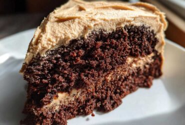 Close-up of a moist, dark slice of gingerbread cake layered with light brown frosting.