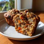 Close-up of a halved morning glory muffin showing moist texture, chunks of carrot, nuts, and raisins inside.