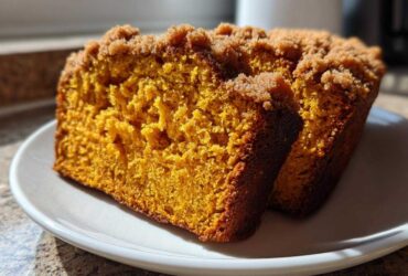 Two slices of vibrant orange, moist pumpkin bread featuring a sugary crumb topping, served on a white plate.