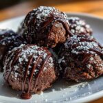 Close-up of several rich, dark pecan pie balls drizzled with chocolate and dusted with powdered sugar.