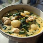 A close-up of a creamy bowl of Olive Garden Chicken Gnocchi Soup featuring tender chicken pieces, soft gnocchi, and wilted spinach.