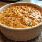 Close-up of a rich, creamy sausage cheese dip served hot in a white bowl with tortilla chips visible.