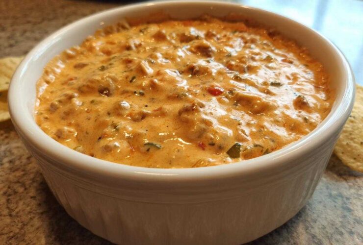 Close-up of a rich, creamy sausage cheese dip served hot in a white bowl with tortilla chips visible.