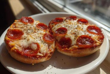 Two freshly baked pepperoni pizza bagels topped with melted cheese and herbs sitting on a white plate.