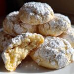 A stack of soft, powdered sugar-dusted cool whip cookies, with one cookie broken open showing the texture.