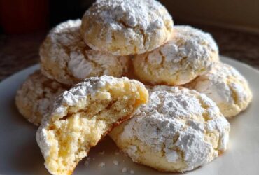 A stack of soft, powdered sugar-dusted cool whip cookies, with one cookie broken open showing the texture.
