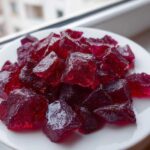A pile of deep red, crystalline chunks of homemade cinnamon rock candy resting on a white plate.