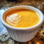 Close-up of creamy, orange-yellow beer cheese dip with spices, served in a small white ramekin.