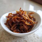 A close-up of deeply browned, glossy caramelized onions piled high in a small white serving bowl.