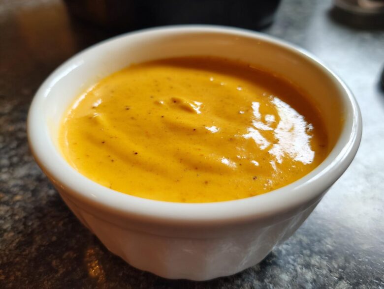 Close-up of smooth, vibrant orange beer cheese dip served in a small white ramekin.