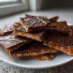 A pile of broken pieces of saltine cracker toffee with a thick layer of caramel and chocolate topping, sprinkled with gold dust.
