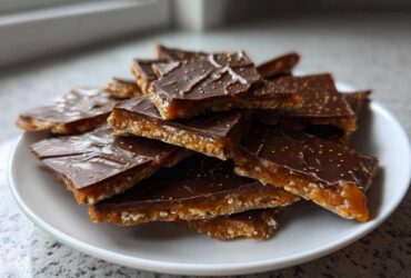 A pile of broken pieces of saltine cracker toffee with a thick layer of caramel and chocolate topping, sprinkled with gold dust.