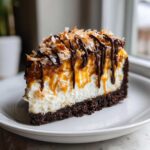 A rich slice of Samoa Cheesecake featuring a dark crust, creamy filling, caramel drizzle, and toasted coconut.