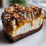 A tall slice of rich Samoa Cheesecake featuring a dark crust, creamy filling, caramel drizzle, whipped cream, and toasted coconut.