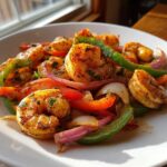 Close-up of seasoned shrimp fajitas mixed with colorful bell peppers and red onions on a white plate.