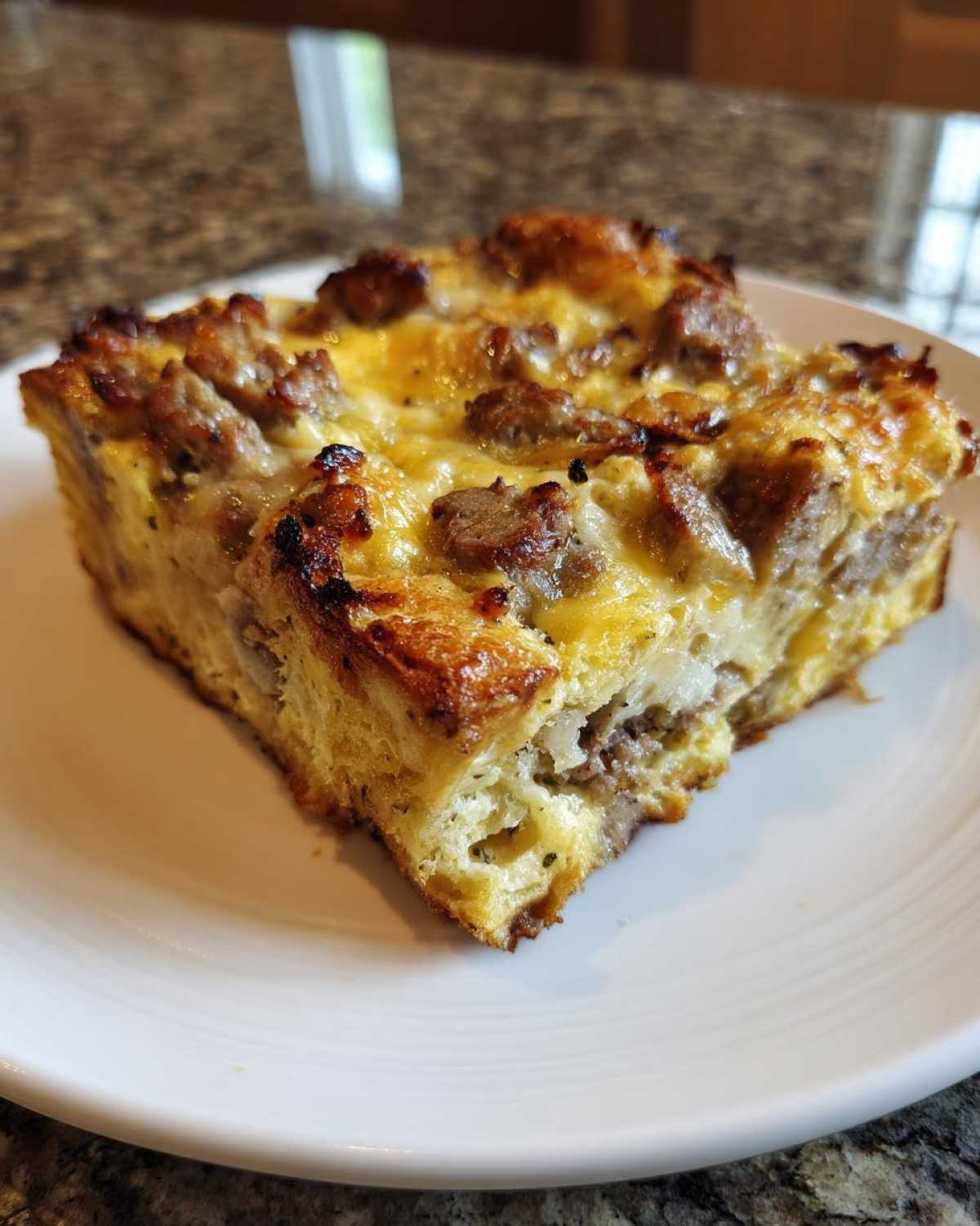 A square slice of savory christmas breakfast casserole with browned sausage and melted cheese on a white plate.