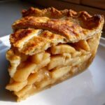 A close-up of a perfect slice of homemade apple pie showing thick apple filling and a golden, flaky lattice crust.
