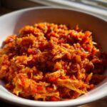 Close-up of shredded chicken in a vibrant orange sauce, representing the slow cooker buffalo chicken chili, served in a white bowl.