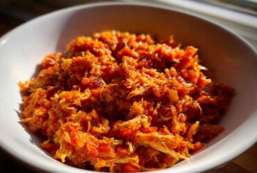 Close-up of shredded chicken in a vibrant orange sauce, representing the slow cooker buffalo chicken chili, served in a white bowl.