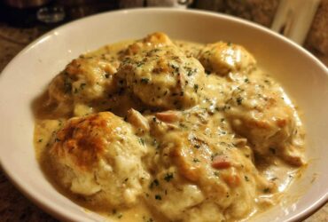 A close-up of a bowl filled with rich, creamy slow cooker chicken and dumplings topped with fresh parsley.