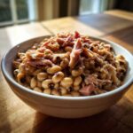 A close-up of a white bowl filled with smoky black eyed peas topped with shredded ham.