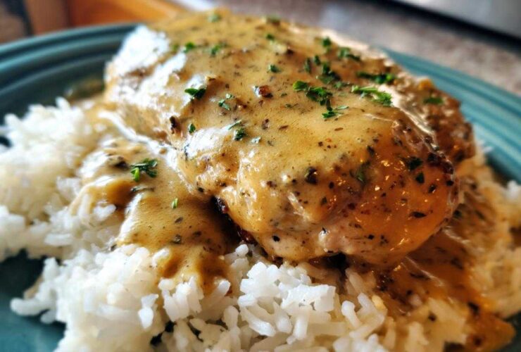 A close-up of smothered chicken and rice, featuring a creamy, seasoned gravy over a chicken breast resting on white rice.