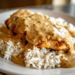 Close-up of a perfectly cooked piece of smothered chicken and rice topped with rich, creamy brown gravy.