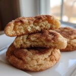 Close-up of a stacked snickerdoodle cookie, broken in half to show the soft, chewy interior and cinnamon sugar coating.