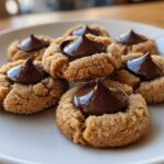Close-up of several soft peanut butter blossoms cookies rolled in sugar, topped with a chocolate kiss.