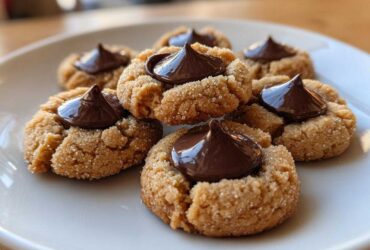Close-up of several soft peanut butter blossoms cookies rolled in sugar, topped with a chocolate kiss.