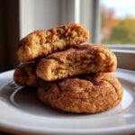 A stack of soft, chewy snickerdoodle cookies, one broken in half showing the texture.